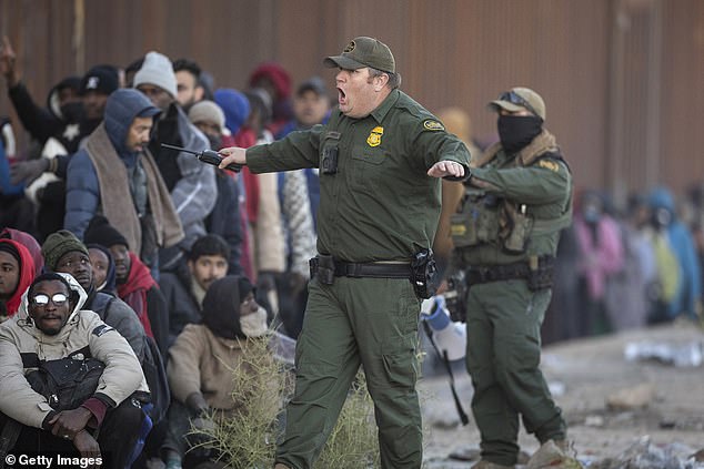 A U.S. Border Patrol agent yells at immigrants who were in a long line of people waiting for transportation from the U.S.-Mexico border on Dec. 6, 2023