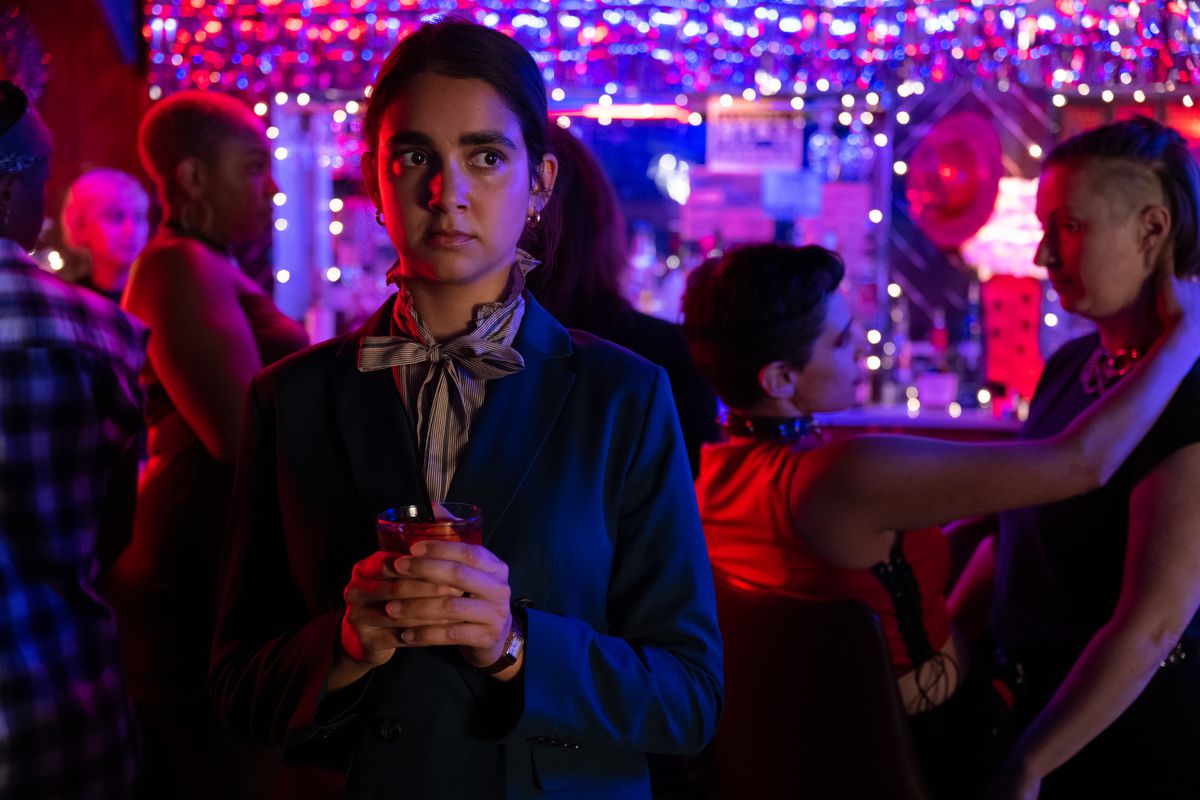 Marian holds her drink with both hands and watches nervously in a lesbian bar scene from Drive-Away Dolls