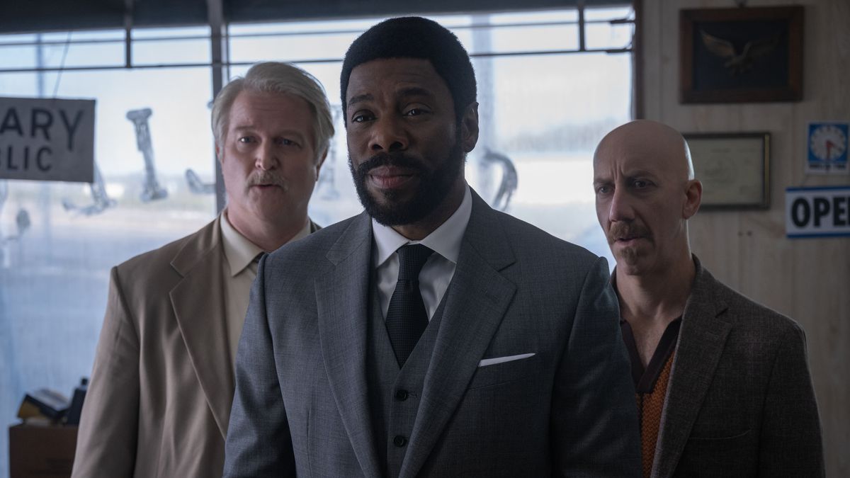 Colman Domingo as The Chief and his two henchmen stand in a car garage in a scene from Drive-Away Dolls. 