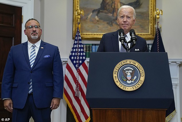 Secretary of Education Miguel Cardona stands next to President Biden in the White House.  The new draft proposal includes several factors that the Secretary may consider to determine whether borrowers face financial hardships that would qualify them for student loan relief.