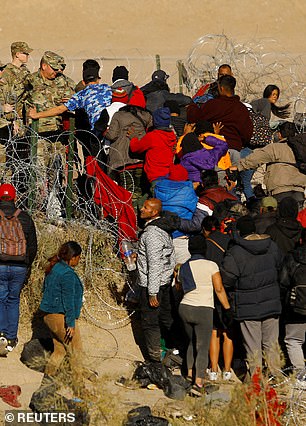 Migrants seeking asylum in the United States attempt to cross a barbed wire fence at the southern border