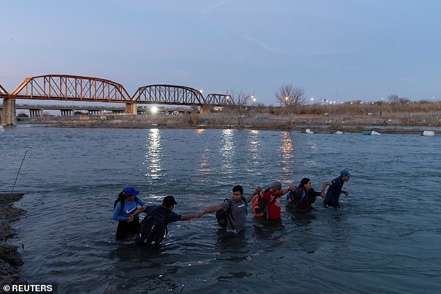 Migrants lock arms with the rest of the group as they wade into the Rio Grande River intending to cross Eagle Pass, Texas, USA, from Piedras Negras, Coahuila, Mexico, February 24, 2024
