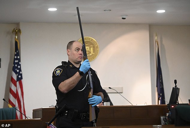 A NYS police officer holds Kevin Monahan's shotgun during summonses in Monahan's murder case