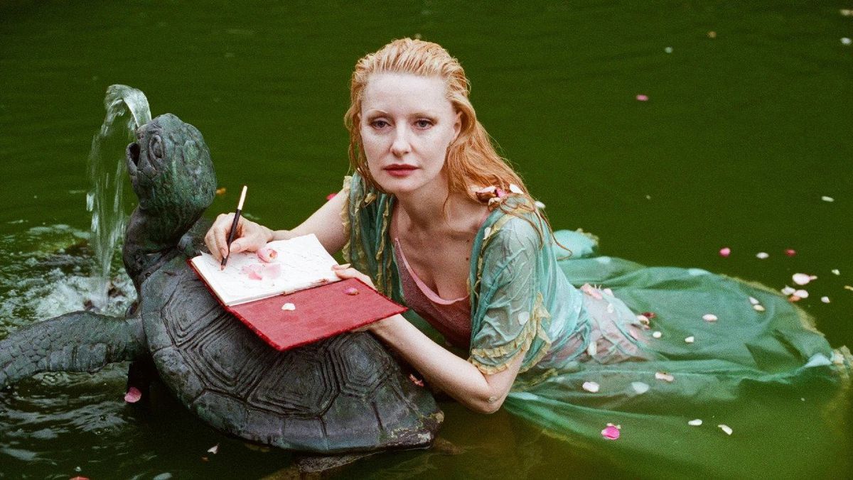 Shere Hite, wearing a light green dress, floats in the water with a notebook open to an image of a turtle.  She looks more than a little like a mermaid.  The image is from the documentary The Disappearance of Shere Hite