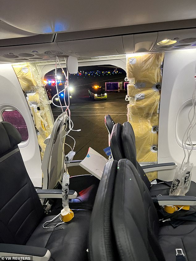 Passenger oxygen masks hang from ceiling panels next to a missing window and part of a side wall of an Alaska Airlines Flight 1282, which was headed to Ontario, California