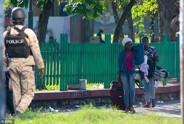 In the photo: A police officer walks by as two people carry their belongings