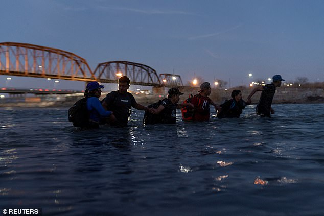 Migrants join arms as they wade into the Rio Grande River last month with the intention of crossing Eagle Pass, Texas