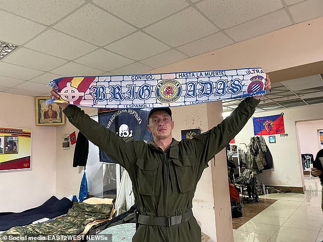 An Española volunteer in military pants holds a scarf that reads 