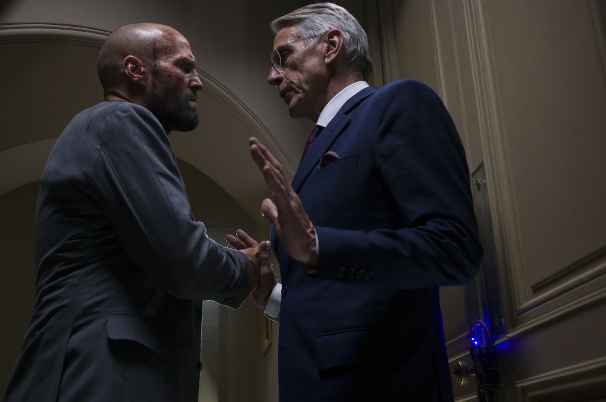 Jason Statham bullies Jeremy Irons, who raises his hands in defense while blocking a door, in The Beekeeper