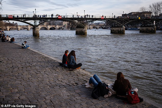 People sit on the banks of the Seine to enjoy the warm weather in front of the Pont des Arts in Paris on February 15, 2024