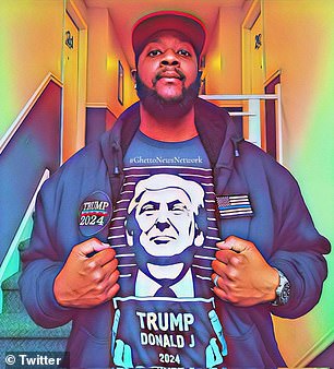 A black man is seen wearing a shirt while Donald Trump holds up a sign and a jacket with a Trump 2024 patch on it