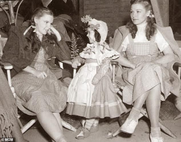 Pictured: Judy Garland sitting with her understudy Caren Marsh Doll and a munchkin on the set of The Wizard of Oz