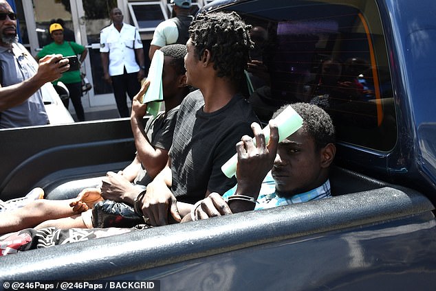 Two of three murder suspects hide their faces with paper in the back of a pickup truck after leaving court.  The person in the middle is another inmate being transported who is not related to the case