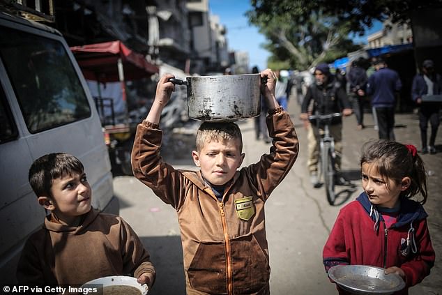 Children carry kitchen utensils as they walk to a food distribution point in Gaza