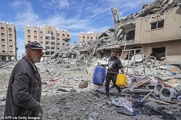 A displaced Palestinian man carries containers amid the rubble of houses destroyed by Israeli bombing in the Hamad area, west of Khan Yunis in the southern Gaza Strip on March 14, 2024