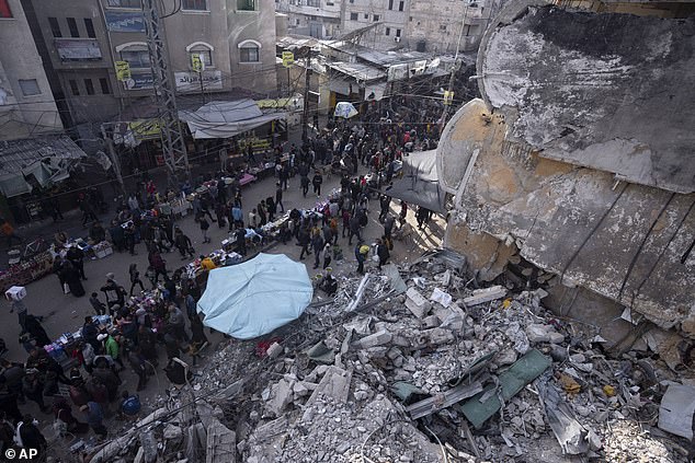 Palestinians shop at a local market next to a residential building destroyed by Israeli airstrikes, during the Islamic holy month of Ramadan, in Rafah, Gaza Strip, Thursday, March 14, 2024