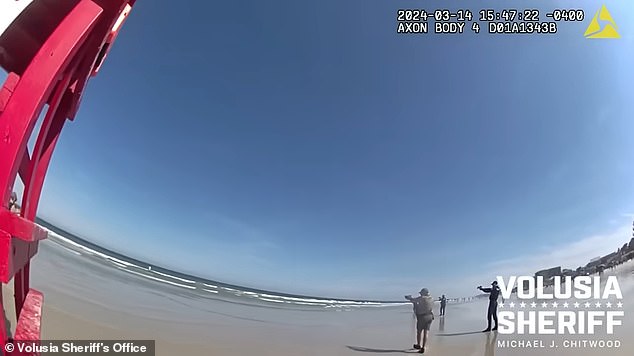 Five officers are seen with guns drawn pointing at Solis-Guzman as he stands in the water at the edge of the beach