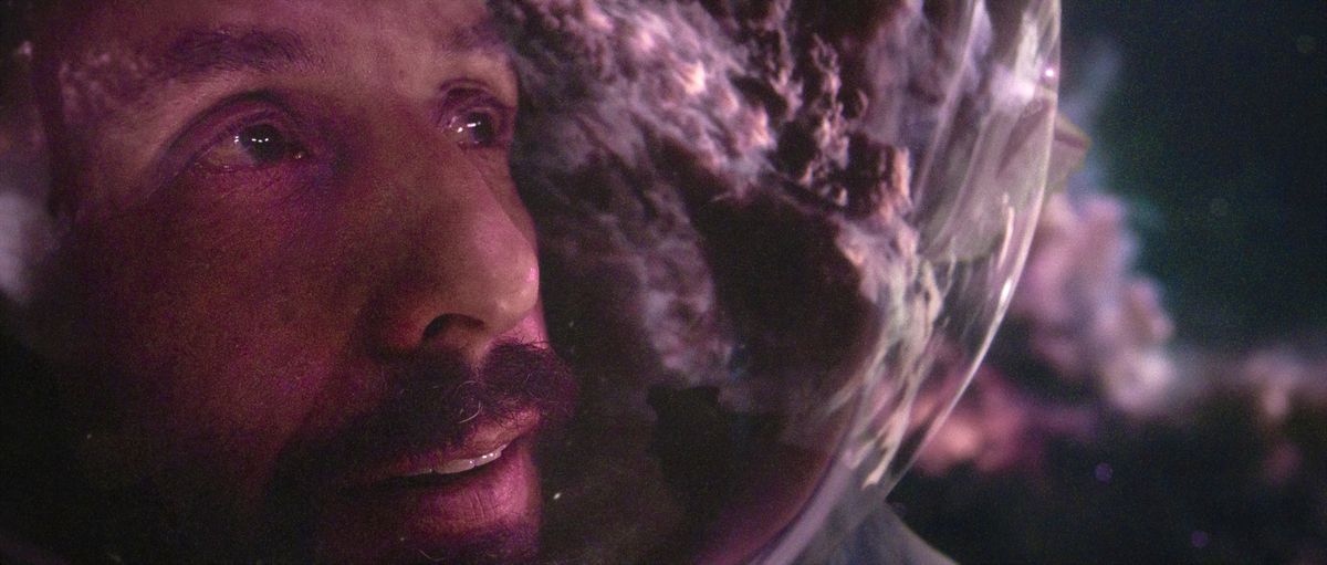 An extreme close-up of the spacesuit-helmeted face of Czech astronaut Jakub (Adam Sandler), with a purple, glowing space cloud reflected in his helmet in Netflix's Spaceman