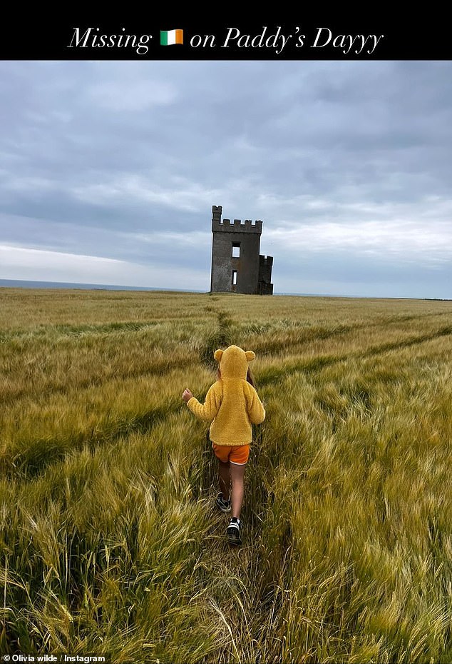 Olivia Wilde, 40, shared a flashback photo of one of her children, wearing orange shorts and a yellow bear jacket, approaching an abandoned castle and used an Irish flag in the message that she 'misses Ireland on Paddy's Dayyy'