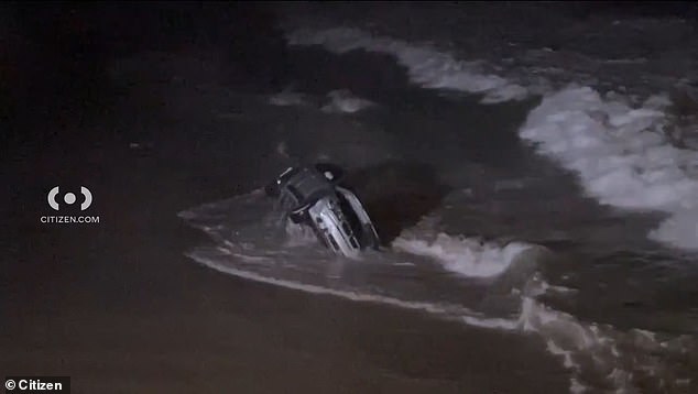 The car rocks in the waves after the woman, who was chased by police, drove the vehicle over the sand and into the water