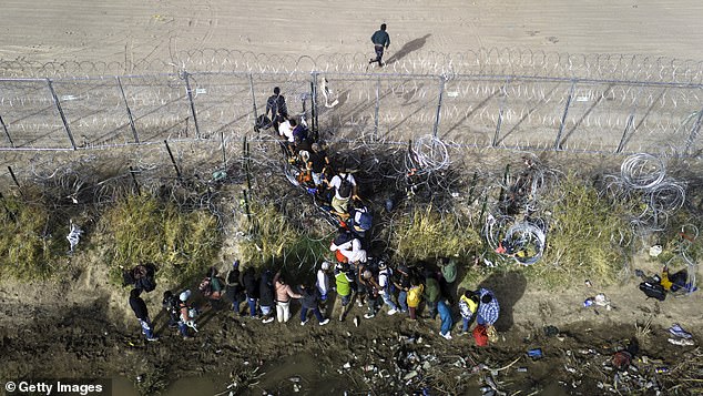 In an aerial photo, immigrants pass through coils of barbed wire as they cross the U.S.-Mexico border on March 13