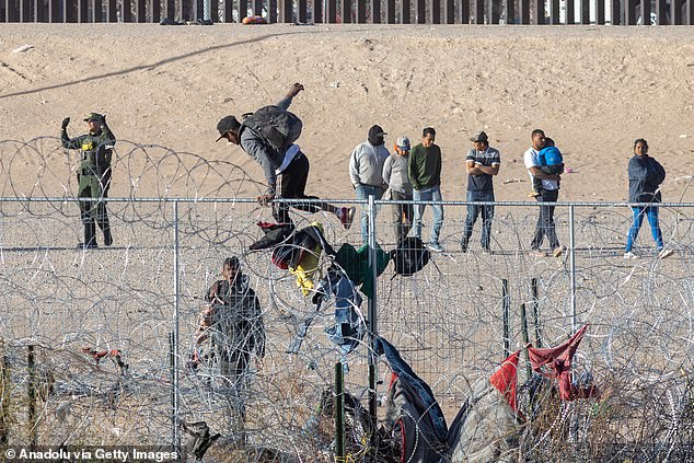 Illegal migrants climb the cyclone fence installed by the Texas National Guard as hundreds of migrants line up along the border wall separating Mexico and the United States awaiting processing