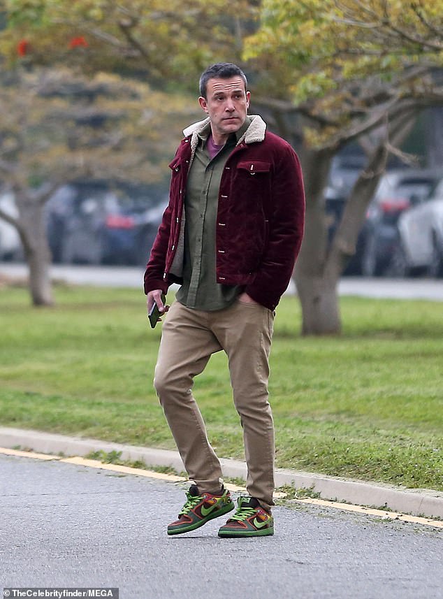 He wore a green button-up shirt over a maroon T-shirt with a maroon corduroy jacket and khaki pants.