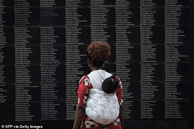 In this file photo taken on April 8, 2019, a woman carrying her child looks at the wall of victims' names as Rwanda marks the 25th anniversary of the 1994 genocide