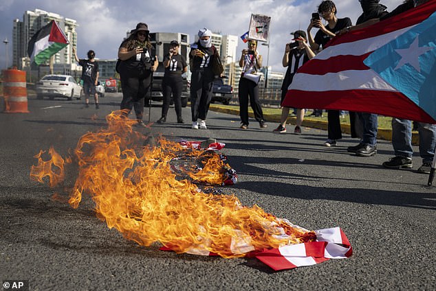 People take photos of an American flag that was set on fire during a protest against the visit of US Vice President Kamala Harris