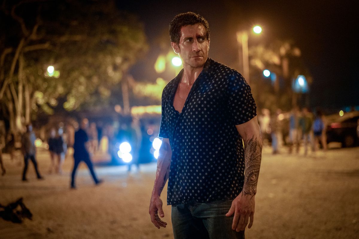 A man in a button-up shirt stands on the street at night.