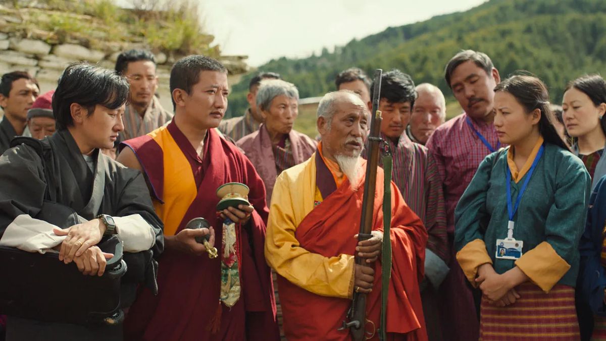 A group of villagers and monks admire an ancient rifle.
