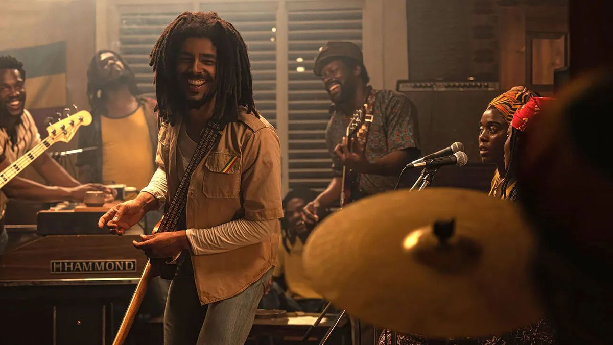 A smiling man with dreadlocks standing next to a group of musicians.