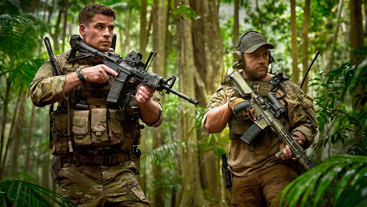 Two men in army camouflage with guns in a tropical forest.