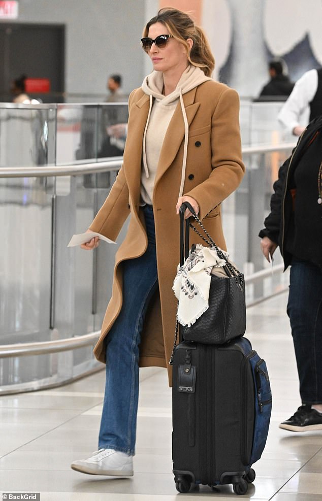 The 43-year-old supermodel wore a beige hoodie under a tan double-breasted trench coat as she pulled her luggage through a terminal before getting ready to board her flight.