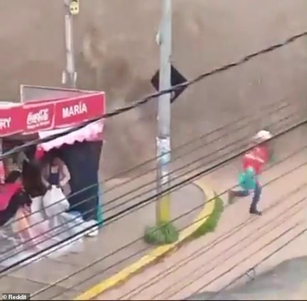 A city worker flees as water flows over a reservoir wall as people remain in a shop in the Bolivian capital La Paz on Wednesday