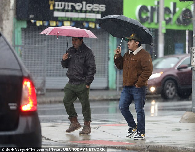 Pedestrians along South Broadway in Yonkers protect themselves from the rain.  The heavy rainfall, which started on Friday evening, is attributed to the merger of two storm systems: one from the north and one from the south.