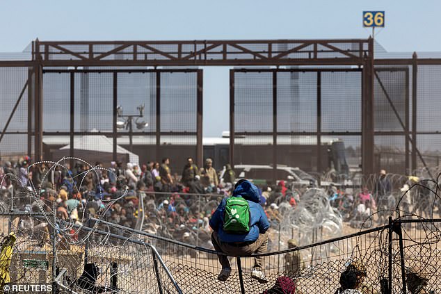 A migrant sits on a fence after a group of migrants fight their way through barbed wire and break through a fence