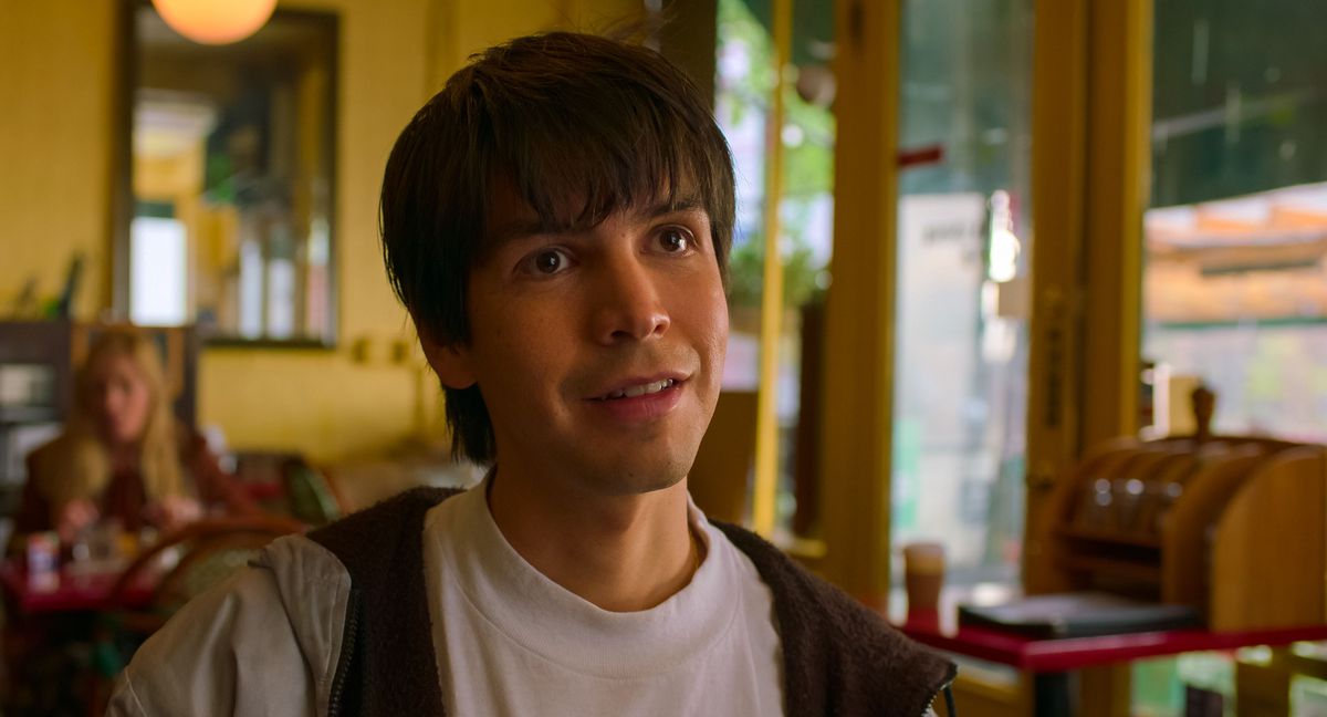 Julio Torres smiles in a hoodie at a New York restaurant in the movie Problemista