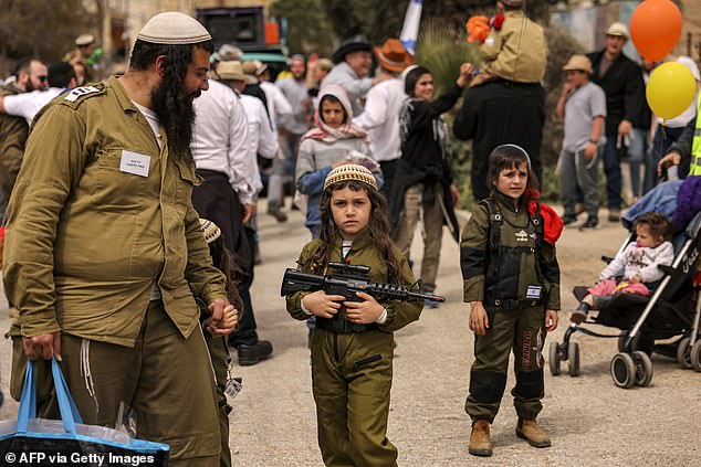 A boy dressed in a Purim costume and holding a toy gun walks along Al-Shuhada Street with other partygoers today