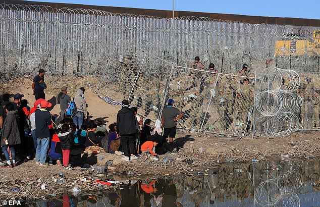 U.S. National Guard personnel strengthen a fence covered in concertina wire near migrants at the border with Mexico on March 23, 2024