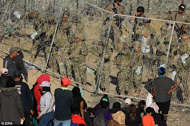 U.S. National Guard personnel strengthen a fence covered in concertina wire near migrants at the border with Mexico, seen from Ciudad Juarez
