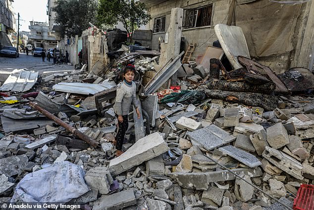 Palestinians, including children, examine the rubble and collect remaining belongings from the rubble of heavily damaged buildings