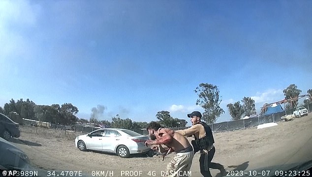 A man holding a gun grabs another man next to a car during an attack by Hamas militants on October 7