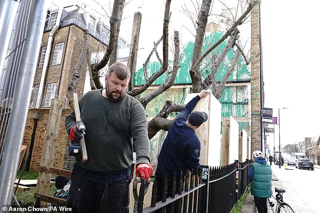 Construction workers erect boarding next to the Banksy artwork on the side of a residential building in Hornsey Road, Finsbury Park