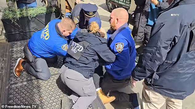 Amid the chaos, a bearded man wearing a brown-colored hoodie was forcefully knocked to the ground by law enforcement officers, who then restrained his hands.