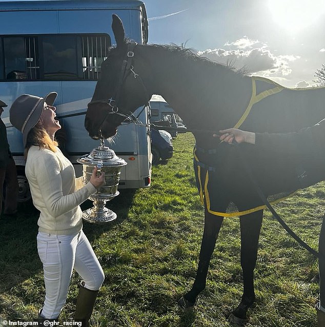 Geri smiles and holds a trophy for her horse Lift Me Up after it wins a race on Easter Saturday