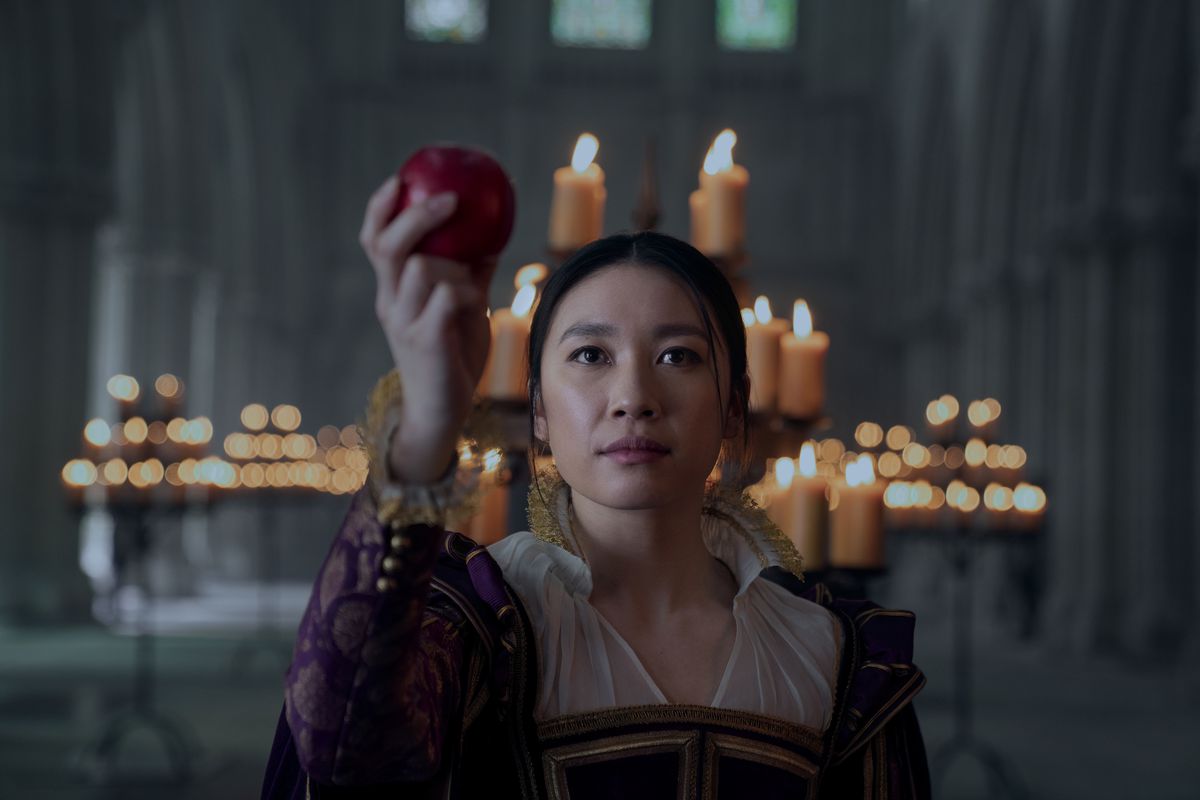 Jess Hong as Jin, dressed in Victorian clothing and holding an apple in a throne room