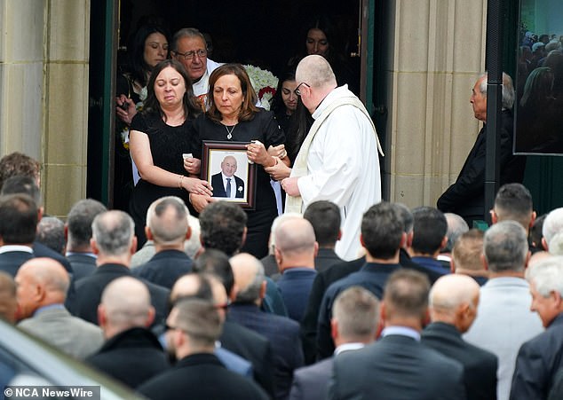 Mourners gather outside St Monica's Catholic Church in Moonee Ponds as family members walk outside with a photo of Latorre following the service