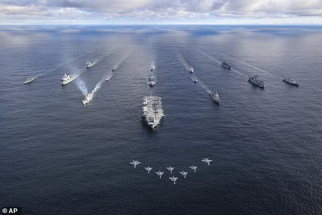 The Royal Navy's aircraft carrier HMS Prince of Wales leads fifteen ship formations as fighter jets fly by at sea for Exercise Nordic Response 24