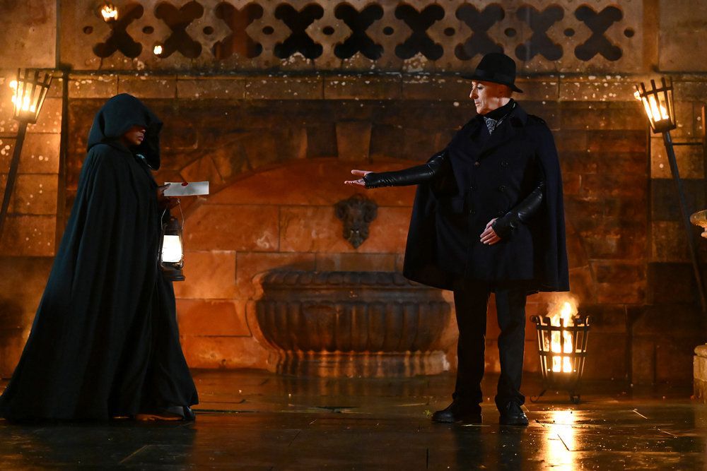 Alan Cumming accepts an envelope from a hooded traitor from The Traitors season 2